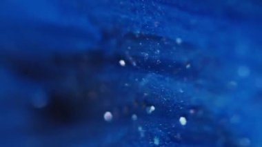 Bokeh sıvısı. Parlak bir geçmişi var. Odaklanmamış mavi mor renkli parlak parlak parlak parlak su sıvı pulları koyu siyah soyutlama üzerinde akıyor..