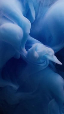 Dikey video. Su sıçraması. Sis dalgası. Sıvı dumanlı akrilik dokuda dönen çözünmüş mavi renkli boya soyut koyu siyah arka planda asılı duruyor..