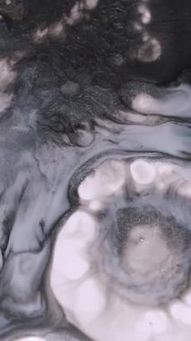 Dikey video. Sıçrama sanatı. Boya damlası. Soyut akrilik mavi arkaplanda yüzen koyu siyah beyaz yuvarlak damlacıklar..