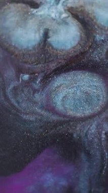 Dikey video. Bulanık mürekkep sıçraması. Parlak pigmentler. Soyut arkaplana yayılan mavi, mor, altın renkli simli sıvılar..