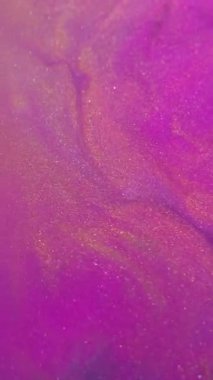 Dikey video. Bulanık boya dökülüyor. Parlak pigmentler. Soyut arkaplana yayılan mor pembe altın renkli simli partiküller..