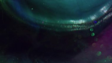 Işıldayan damlalar. Bulanık sıvı karışımı. Yuvarlak kürede yeşil mavi sıvı dökülmesi. Suyun altındaki renk pigmenti soyut mor arkaplanı çözüyor.