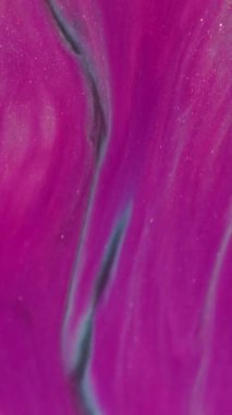 Dikey video. Sıvı dökülmesi. Akrilik sıçrama. Soyut arkaplana yayılan parlak parçacıkların odağından çıkarılmış pembe altın renkli simler..