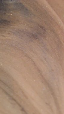 Dikey video. Nehir boyası. Işıl ışıl. Odaklanamayan sarı mor renkli simli parçacıklar soyut akrilik zemin üzerine dökülür..