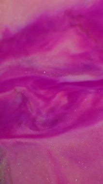 Dikey video. Bulanık boya sıçraması. Parlak pigmentler. Soyut arkaplana yayılan mor pembe altın renkli simli partiküller..