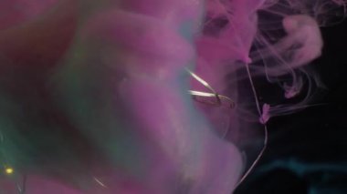 Odaklanmamış duman damlası. Parlayan ampul. Aydınlatılmış cam çelenk soyut renk sıçraması. Siyah arkaplanda pembe mavi bulut akışı.