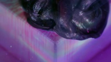 Yüzen boya. Odaklanmamış sanat sıçraması. Işıldayan mürekkep menekşe siyah akış küpü. Suyun soyut arka planında mor boya çözünüyor.