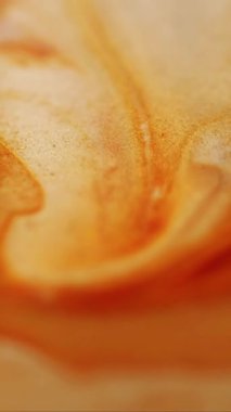 Dikey video. Enamel sıvısı. Pırıl pırıl. Soyut akrilik zemin üzerine dökülen su lekelerinde çözünmüş sarı turuncu renkli boya..