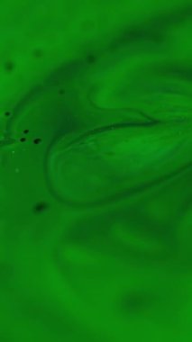 Dikey video. Yağ damlası. Dalgalanma arka planı. Odaklanmamış yeşil renkli parlak doku sanat soyutlaması üzerinde yüzen boya suyu sıçratır.