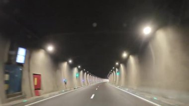 Boş, modern bir otoban tünelinde çekilen bir bakış açısı. Aydınlatılmış beton duvarlar ve sonunda ışık olan asfalt yol