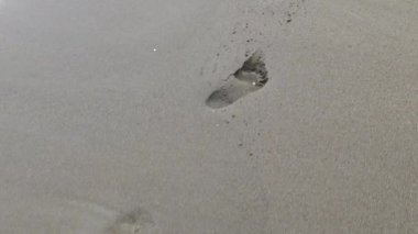 Köpüklü beyaz köpüklü yumuşak okyanus dalgaları nemli kumlu sahilden insan ayak izlerini nazikçe siliyor. Hafıza kaybının, zamanın geçişinin ve varoluşun geçici doğasının gösterişli temaları.