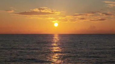 Sakin okyanusun üzerinde altın gün doğumu, su yüzeyine çarpıcı bir ışık oyunu sergiliyor. Deniz manzarası huzurlu, bulutlar gökyüzüne dağılmış.