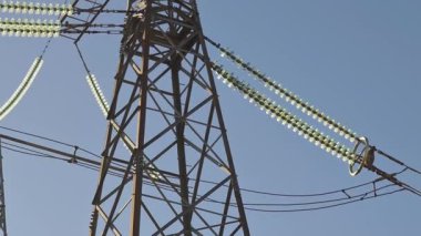 Yüksek voltaj iletim kulesinin detaylı bir görüntüsü. İçinde cam yalıtıcılar var. Karmaşık çelik kafes tasarımından canlı mavi gökyüzüne karşı kurulmuş elektrik hatlarına geçiş yapıyor.