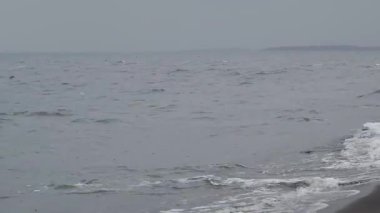 Bulutlu gökyüzü, yağmurun dalgalı sulara karıştığı fırtınalı deniz manzarasının dramatik ve kasvetli atmosferini güçlendirir.