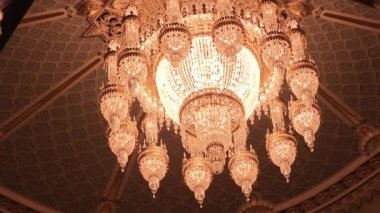 Görkemli kristal avize sıcak, altın bir parıltı saçıyor. Süslü bir tavandan sarkan karmaşık detaylarla süslü aydınlatma armatürü. Tiflis, Gürcistan - 12 Şubat 2026.