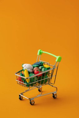 Sarı arka planda yemek için sepetteki oyuncak sebzeler.