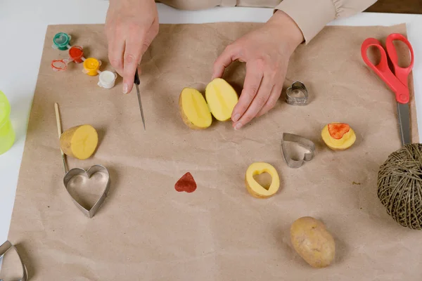 Sello de patata en forma de corazón en papel artesanal. El proceso de decorar un regalo para el Día de San Valentín. Preparándose para la celebración del 14 de febrero. — Foto de Stock