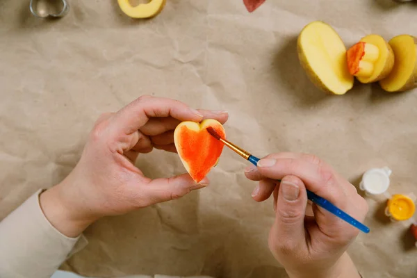 Sello de patata en forma de corazón en papel artesanal. El proceso de decorar un regalo para el Día de San Valentín. Preparándose para la celebración del 14 de febrero. — Foto de Stock