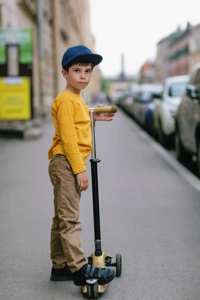 Chlapec na dětském skútru. Portrét dítěte ve městě na ulici. — Stock fotografie