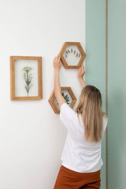 Kadın, kurumuş çiçekleri çerçeveyle süslüyor. Botanik yapraklı duvarlar. Çevre dostu boho dekor. Gerçek insanların kişisel alanı. 
