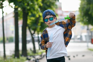 Kasabada güneş gözlüğü takan bir çocuk. Bebek sabun köpüğüyle oynuyor