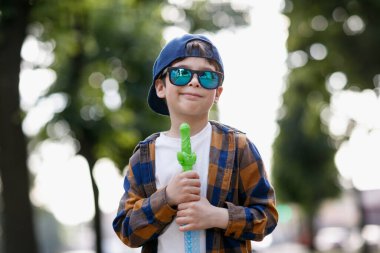 Kasabada güneş gözlüğü takan bir çocuk. Bebek sabun köpüğüyle oynuyor