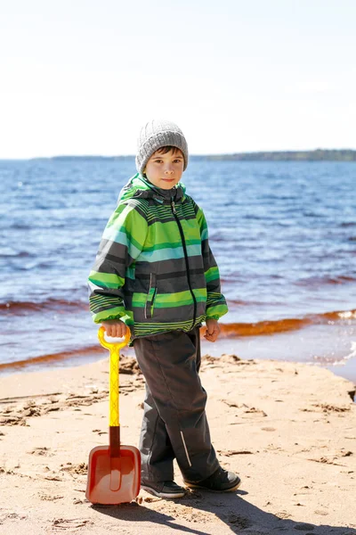 Chlapec v bundě s lopatou na pláži — Stock fotografie