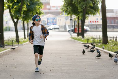 Çocuk güvercinlerle oynuyor. Yürüyüşe çıkmış güneş gözlüklü bir çocuk.