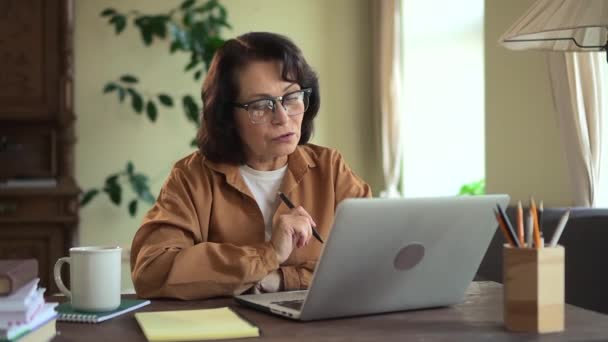 Geschäftsfrau unterhält sich online und sitzt mit Laptop am Tisch im Home Office.