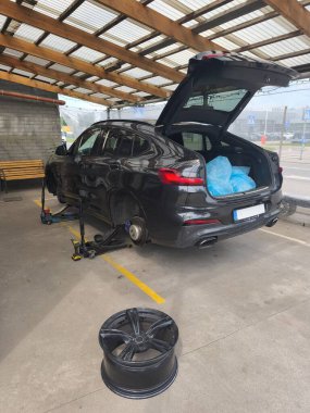 Lastik servisi ve sezonluk hazırlık: bir lastik atölyesinde lastiklerin değiştirilmesi sırasında kriko üzerindeki modern araba tekerleksiz duruyor