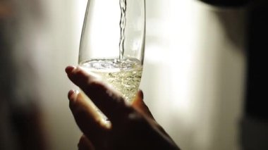 Şampanya şişeden cama dökülür. Köpükler ve köpükler su bardağında yükselir. Şampanya ile kristal bardak. Kadın eli bardak getirir ve şampanya içer. Bir bardak baloncuklu beyaz şarap..