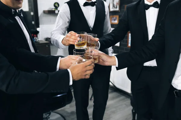 Slibní mladí muži slaví a pijí whisky. Nejlepší muži s brýlemi plnými alkoholických nápojů oblečených ve formálních šatech. Stock Obrázky