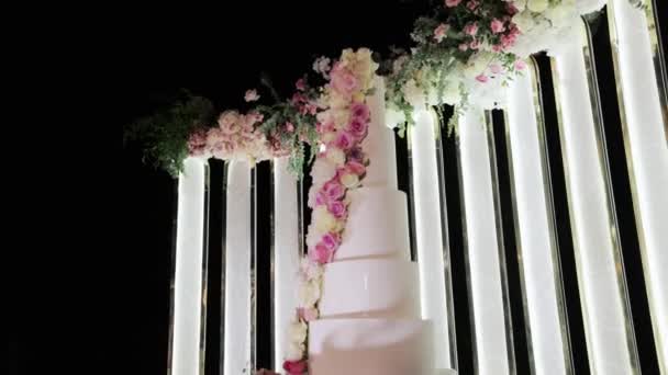 Wedding cake with flowers on the table. White fruit wedding cake on a wedding party night. Wedding arch with flowers on wedding day. — Stock Video