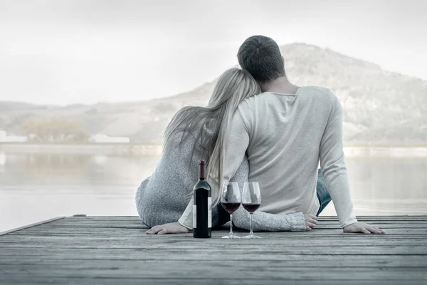 Пара сидящих на пирсе с красным вином — стоковое фото
