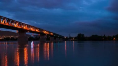Günbatımından sonra Tuna Nehri ve Budapeşte Macaristan 'daki tren köprüsü üzerindeki hızlandırılmış manzara bulutlu bir gecede tekneler ve gemilerle birlikte..
