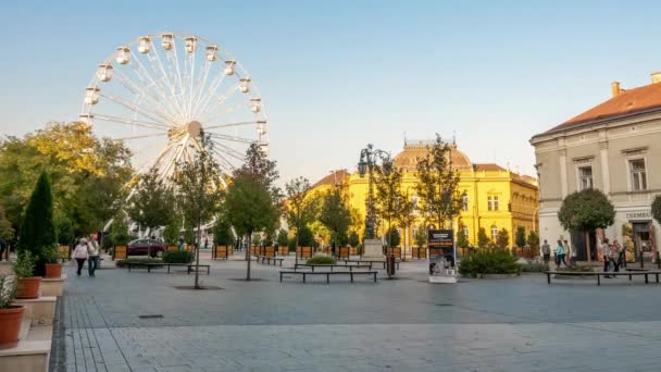 SZEKESFEHERVAR, HUNGRÍA - 26 DE OCTUBRE DE 2019: Vista temporal de la noria en el parque Zichy y la gente caminando por las calles de Szekesfehervar, Hungría en un día de otoño. — Vídeo de stock