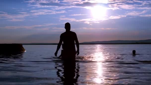 Widok na sylwetkę ludzi pływających i spacerujących w jeziorze Velence podczas zachodu słońca w lecie na Węgrzech. — Wideo stockowe