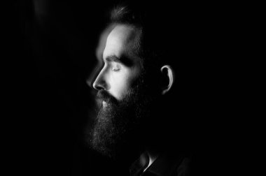 Stüdyoda sakallı bir adamın portresi. Önünde siyah bir arka plan ve dramatik bir ışık var..