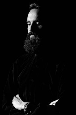 Stüdyoda sakallı bir adamın portresi. Önünde siyah bir arka plan ve dramatik bir ışık var..