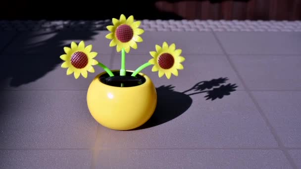 Zicht op een kunstmatig op zonne-energie werkende kunststof zonnebloem die door het zonlicht op een tafel in de tuin beweegt en hernieuwbare energiebronnen voorstelt. — Stockvideo