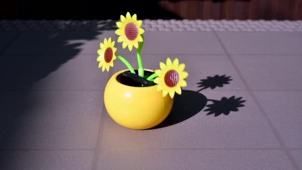 Vedere pe o floarea-soarelui artificială din plastic alimentată cu energie solară care se deplasează prin lumina soarelui reprezentând sursa de energie regenerabilă pe o masă din grădină . — Videoclip de stoc