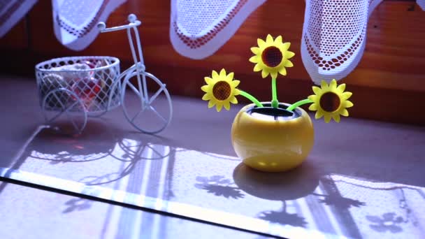 Vista sobre um girassol artificial de plástico movido a energia solar movendo-se pela luz solar que representa fonte de energia renovável na janela. — Vídeo de Stock