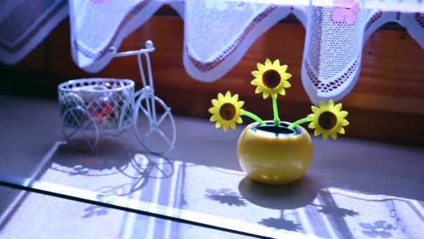 Güneş enerjisiyle çalışan plastik bir ayçiçeğinin güneş ışığında hareket edişine bakın. Pencerede yenilenebilir enerji kaynağını temsil ediyor.. — Stok video
