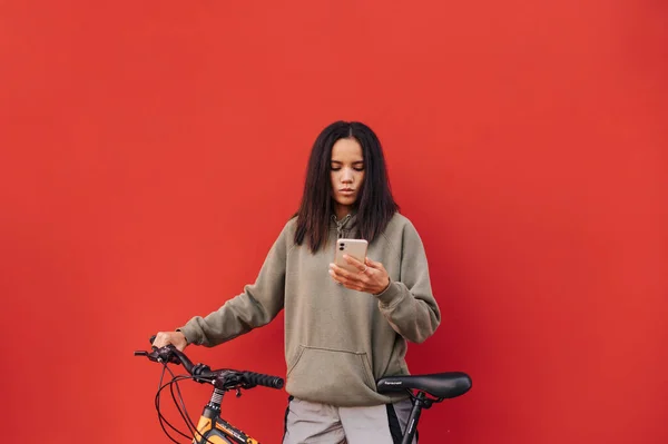 美丽的他惊慌失措的女人站在一辆红色背景的自行车上 用的是一张严肃面孔的智能手机 生态交通 — 图库照片