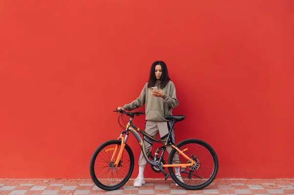 Красивая Женщина Спортивной Одежде Стоит Велосипедом Фоне Красной Стены Использует — стоковое фото
