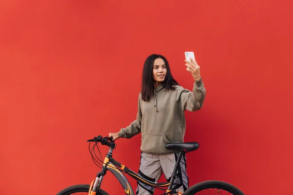 Ευτυχισμένη Γυναίκα Κομψά Ρούχα Στέκεται Ένα Ποδήλατο Φόντο Κόκκινου Τοίχου — Φωτογραφία Αρχείου