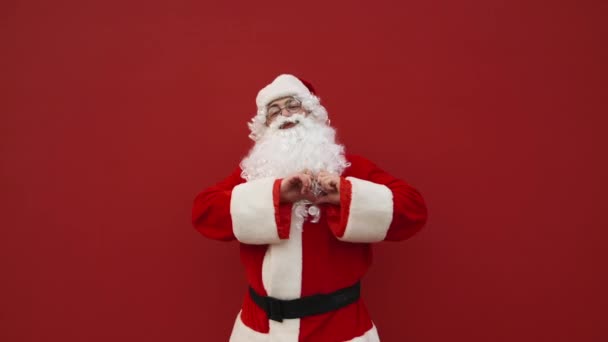 快乐的圣诞老人站在红色的背景上看着摄像机 脸上挂着微笑 展示着他内心的姿态 圣诞节的概念和爱桑塔 — 图库视频影像