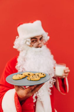 Noel Baba kırmızı arka plandaki bir şişeden kola içiyor. Dikey