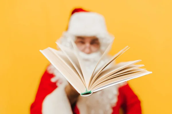 黄色の背景に隔離された彼の手の中に開いている本とサンタ クリスマスの願いの本 — ストック写真