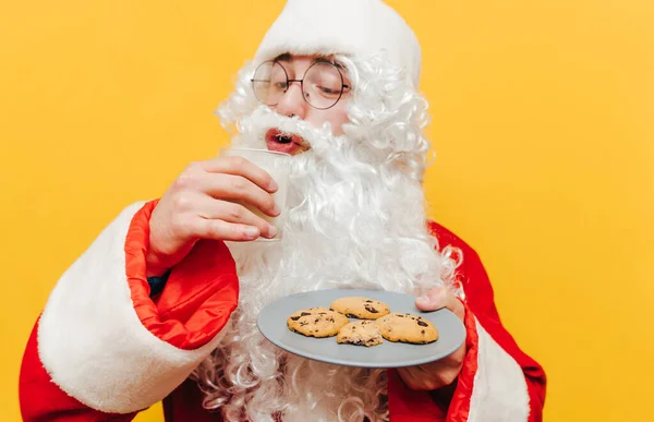 클로스가 우유를 마시고 노란색 배경으로 초콜릿 크리스마스 쿠키를 먹으며 사진을 — 스톡 사진